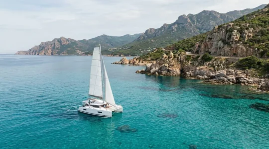 Catamaran naviguant le long des côtes rocheuses corses aux eaux turquoise